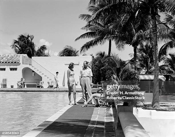 1930s MAN AND THREE WOMEN STANDING SITTING TALKING AROUND SWIMMING POOL MIAMI BEACH FLORIDA USA