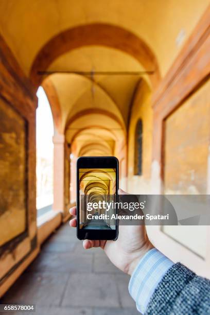 close up of a hand holding smartphone taking picture of porticos in bologna, italy - virtual vacations stock pictures, royalty-free photos & images