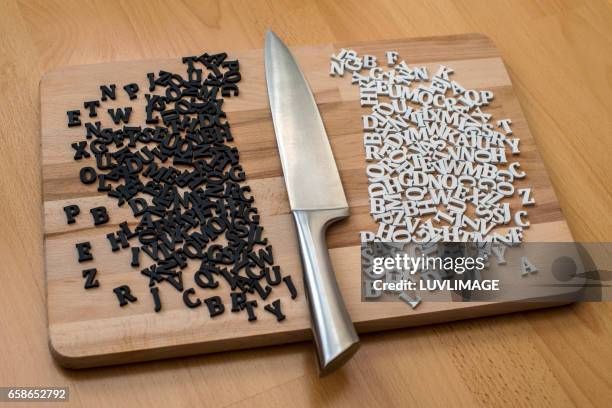 a cutting board with a knife between black and white letters. - discrimination stock-fotos und bilder