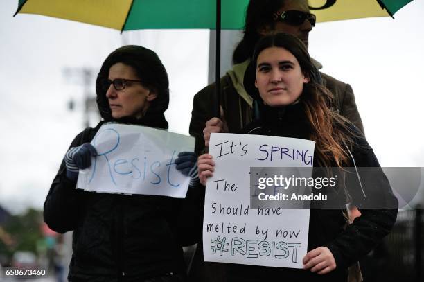 Women hold banners reading "Resist - It's spring, the I.C.E should have melted by now" during a protest outside the Immigration and Customs...