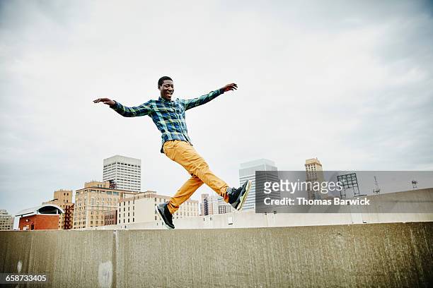 man dancing on top of wall on rooftop - control pants foto e immagini stock