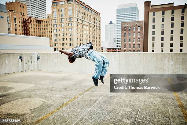 man doing a backflip on rooftop of building - fare le capriole all'indietro foto e immagini stock