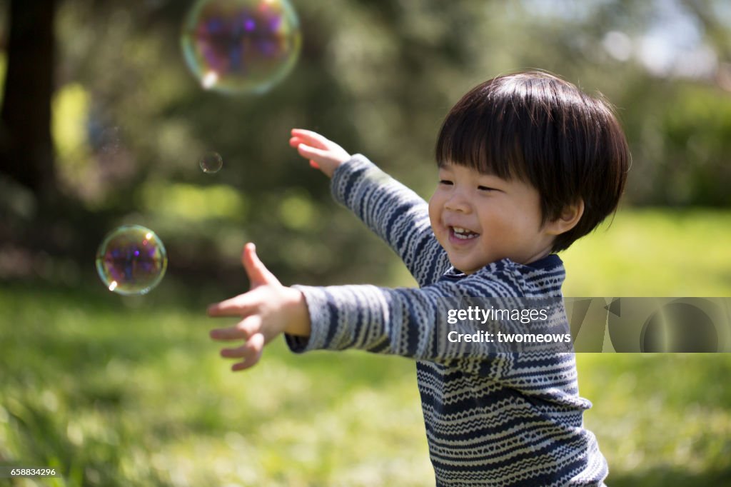 Asian toddler catching soap bubble.