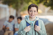Smiling schoolboy standing with schoolbag in campus