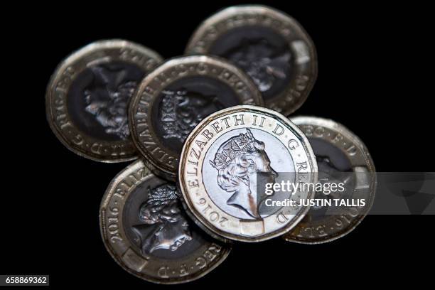 In this posed photograph, newly issued 12-sided £1 coins are pictured in a pile in London on March 28, 2017. Britain's new £1 coin with the symbols...