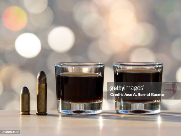 glass of crystal of chupito fill of an alcoholic drink and a bullet of pistol, , illuminated by the light of the sun - bebida stockfoto's en -beelden