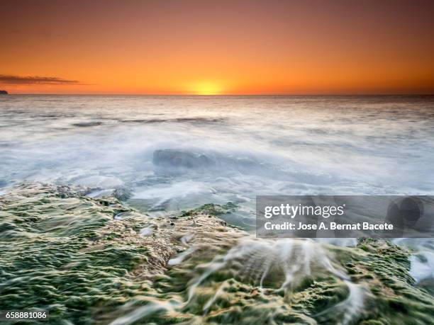 exit of the sun of orange color, on the surface of the sea, in a zone of coast with rocks and waves in movement - clima tropical stock pictures, royalty-free photos & images