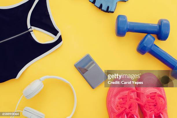 flat lay shot of woman sport equipment, shoes, water, earphone and phone on yellow background - running gear stock-fotos und bilder