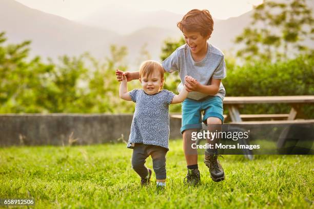 happy boy playing with toddler on grassy field - sibling stock pictures, royalty-free photos & images