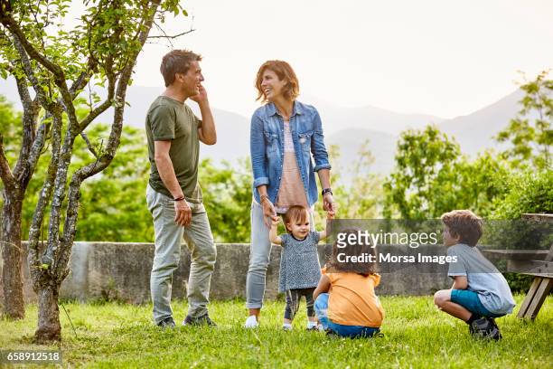 happy parents talking while kids playing on field - family with three children foto e immagini stock
