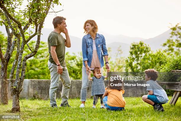 gelukkige ouders praten terwijl de kinderen spelen op veld - child standing talking stockfoto's en -beelden