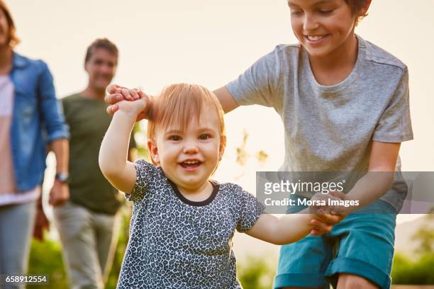 happy children playing with parents in background - baby brother stock pictures, royalty-free photos & images