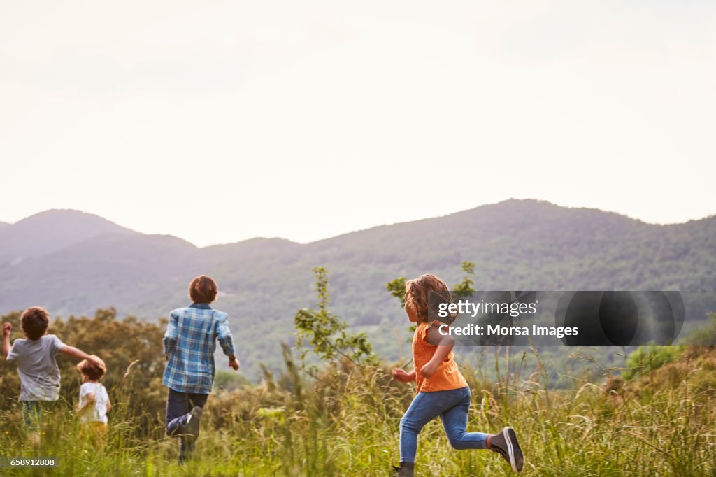Children running on grassy field against clear sky