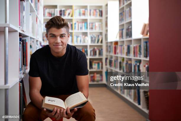 portrait of male student holding book in library - teenager reading a book stock pictures, royalty-free photos & images