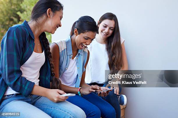 students laughing and looking at phone - 3 teenagers mobile outdoors stock-fotos und bilder