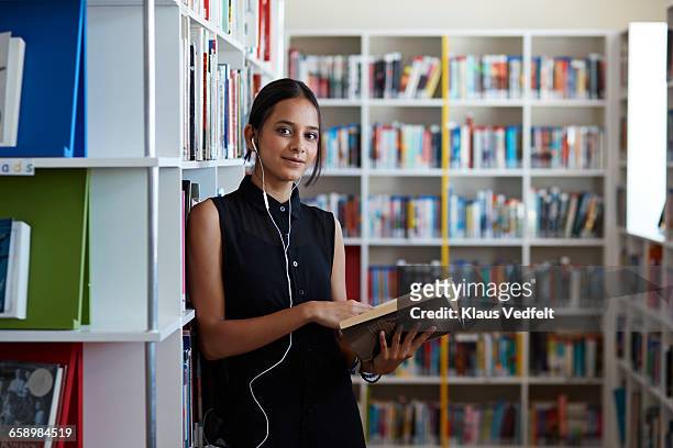 portrait of female student holding book in library - teenagers reading books stock pictures, royalty-free photos & images