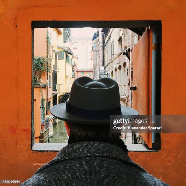 man in hat looking at the canal through the window in bologna, italy - bologna italy stock pictures, royalty-free photos & images