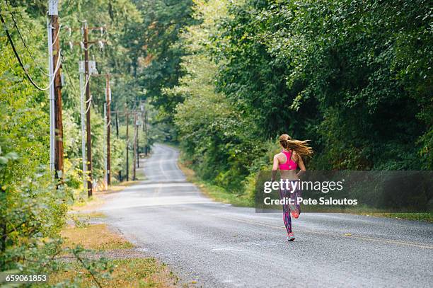 rear view of teenage female runner running down rural road - girls in leggings stock-fotos und bilder