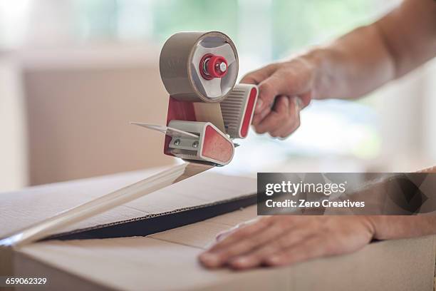 man taping up box using tape dispenser, close-up - tape dispenser stock pictures, royalty-free photos & images