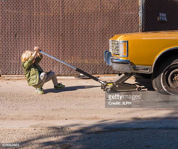 boy using car jack to raise car - car jack stock-fotos und bilder