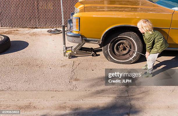 boy removing wheel nuts from flat tyre - flat tyre stockfoto's en -beelden