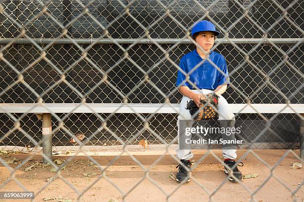 boy sitting on bench behind wire fence at baseball practise - sports field fence stock pictures, royalty-free photos & images