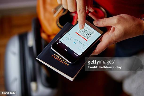 woman holding passport and smartphone, smartphone showing qr code, overhead view - bordkarte stock-fotos und bilder