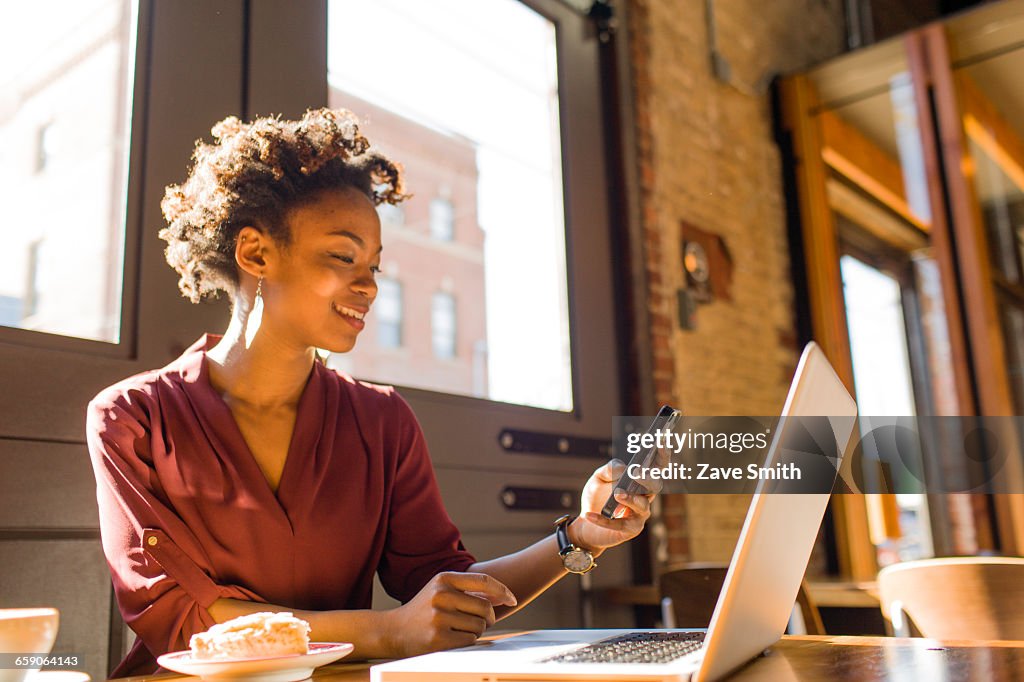 Young businesswoman sitting in cafe, using laptop and smartphone