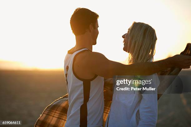 couple on beach, at sunset, man putting blanket around young woman - caballerosidad fotografías e imágenes de stock