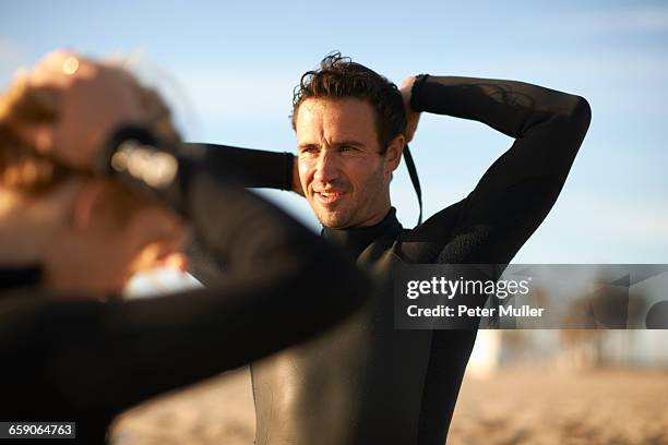 surfing couple zipping up wetsuits on venice beach, california, usa - wetsuit stock pictures, royalty-free photos & images