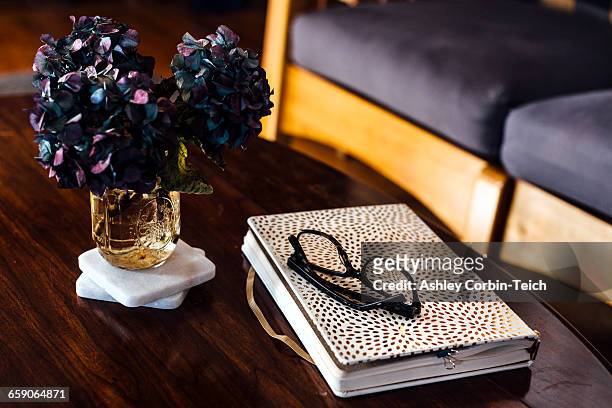 book, reading glasses and flower arrangement on coffee table - coffee table books stockfoto's en -beelden