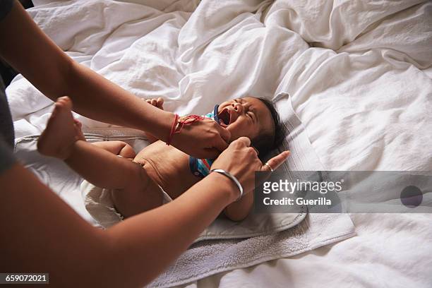 mother dressing crying baby boy lying on changing mat - baby clothes - fotografias e filmes do acervo