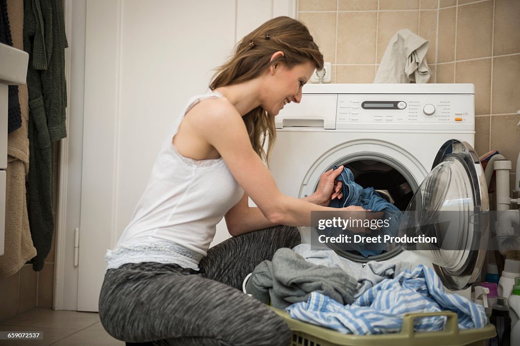 Young woman taking laundry out of washing machine, Munich, Bavaria, Germany