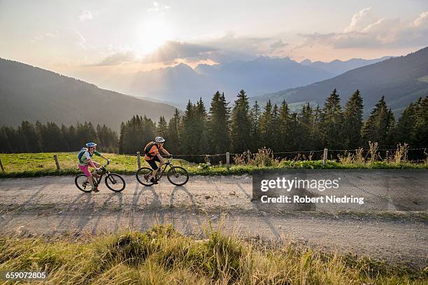 elevated view of mountain bikers riding on dirt road during sunset, zillertal, tyrol, austria - fahrradausflug stock-fotos und bilder