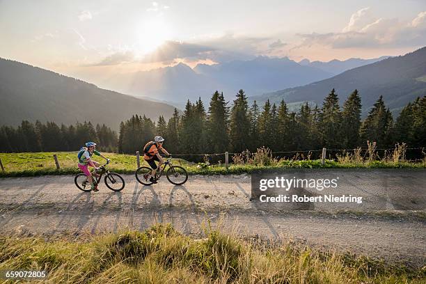 elevated view of mountain bikers riding on dirt road during sunset, zillertal, tyrol, austria - zillertal stock pictures, royalty-free photos & images