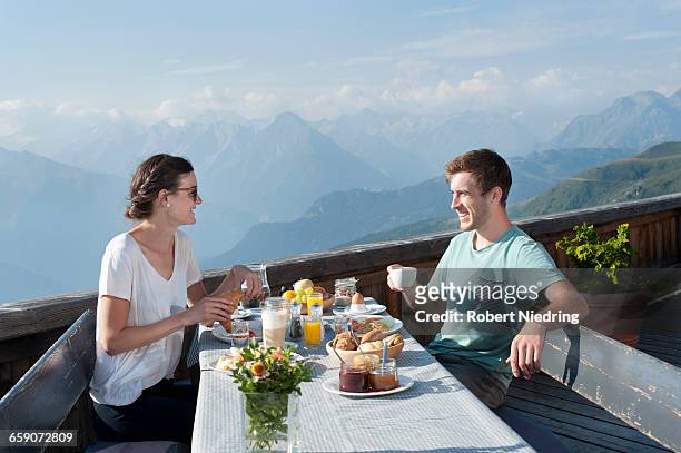 young couple eating breakfast on terrace and smiling, zillertal, tyrol, austria - té terraza fotografías e imágenes de stock