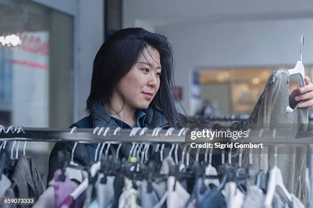 young woman choosing clothes from clothes rack in clothing store, freiburg im breisgau, baden-württemberg, germany - clothes hanging on rack at store for sale foto e immagini stock