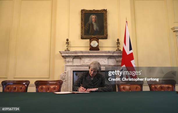 British Prime Minister Theresa May in the cabinet, sitting below a painting of Britain's first Prime Minister Robert Walpole, signs the official...