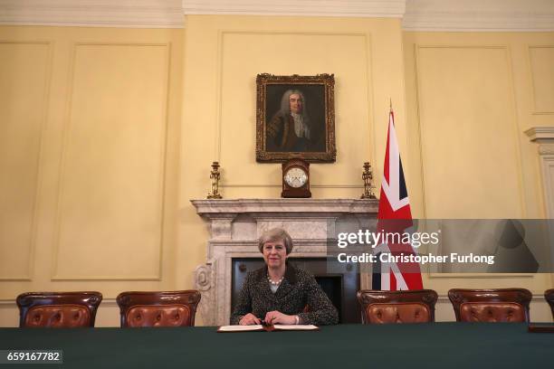 British Prime Minister Theresa May in the cabinet, sitting below a painting of Britain's first Prime Minister Robert Walpole, signs the official...