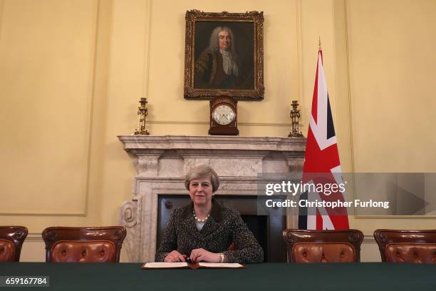 British Prime Minister Theresa May in the cabinet, sitting below a painting of Britain's first Prime Minister Robert Walpole, signs the official...