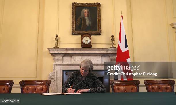 British Prime Minister Theresa May in the cabinet, sitting below a painting of Britain's first Prime Minister Robert Walpole, signs the official...
