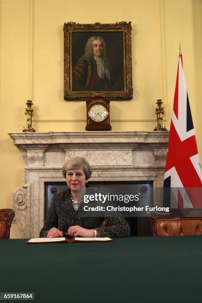 British Prime Minister Theresa May in the cabinet, sitting below a painting of Britain's first Prime Minister Robert Walpole, signs the official...