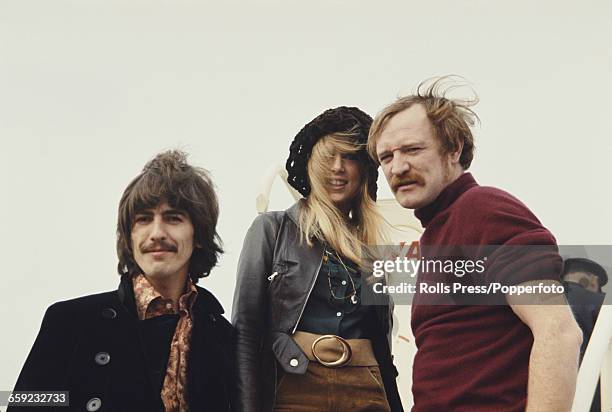 George Harrison , guitarist with the Beatles, pictured with his wife Pattie Boyd and actor Richard Harris as they climb steps up to an aeroplane at...