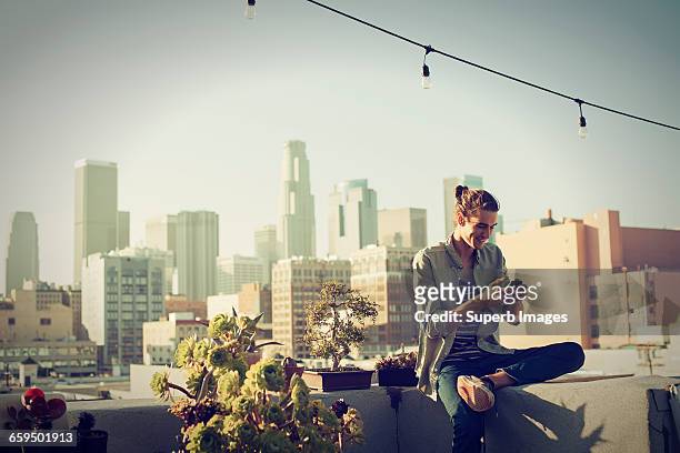 young man checking his smartphone on urban rooftop - city of los angeles stockfoto's en -beelden