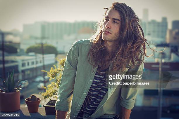 young man on urban rooftop - langes haar stock-fotos und bilder
