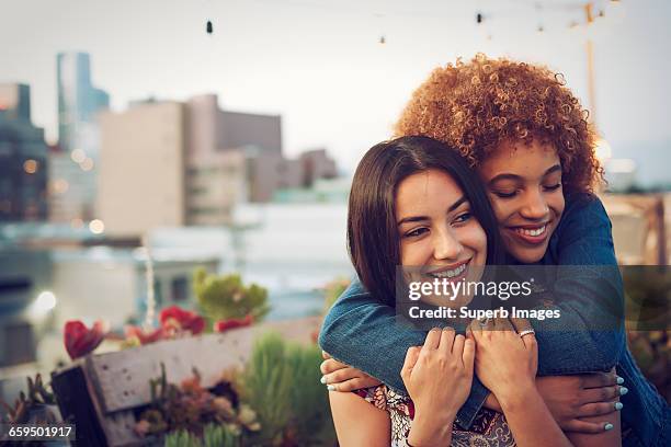 friends hugging on urban rooftop - amistad femenina fotografías e imágenes de stock