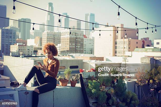 young woman checking smartphone on urban rooftop - california cities foto e immagini stock