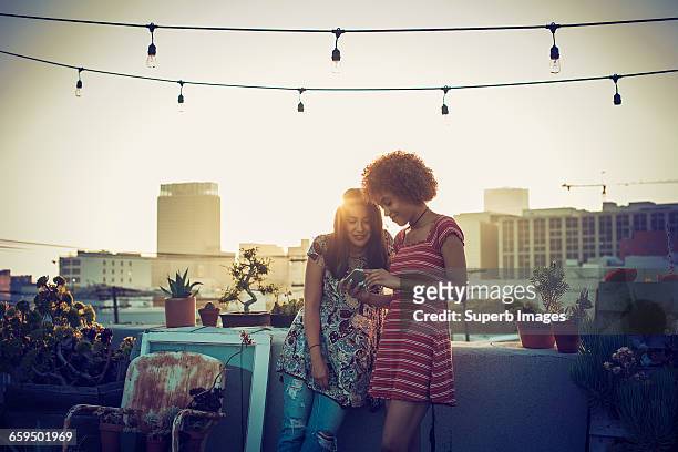 friends sharing smartphone on urban rooftop - buildings side by side stock pictures, royalty-free photos & images