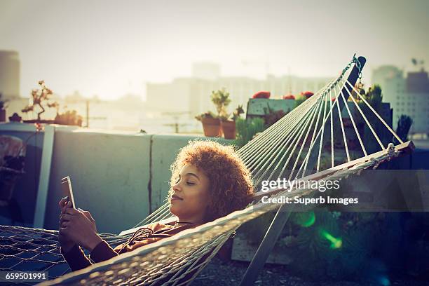 young woman checks smartphone from hammock - hängematte stock-fotos und bilder