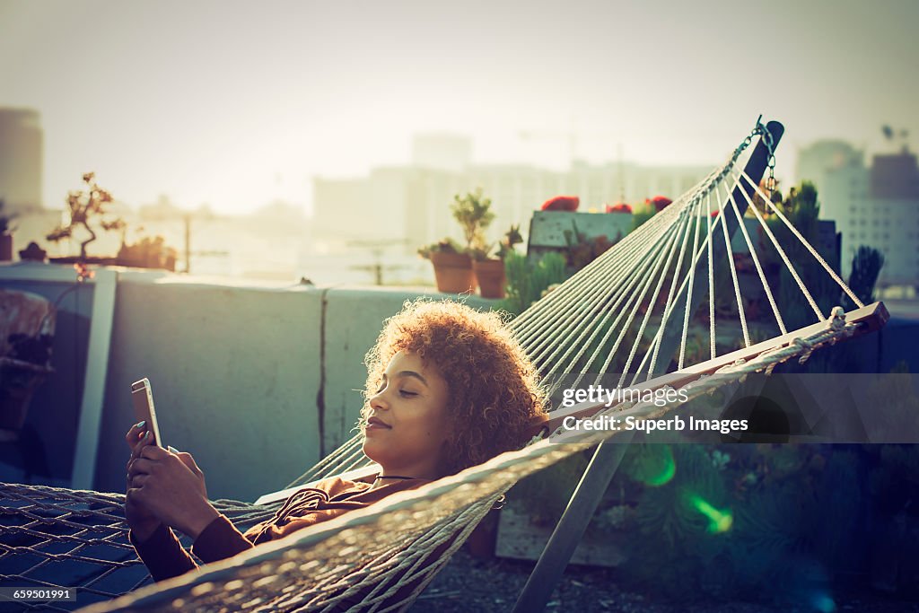 Young woman checks smartphone from hammock